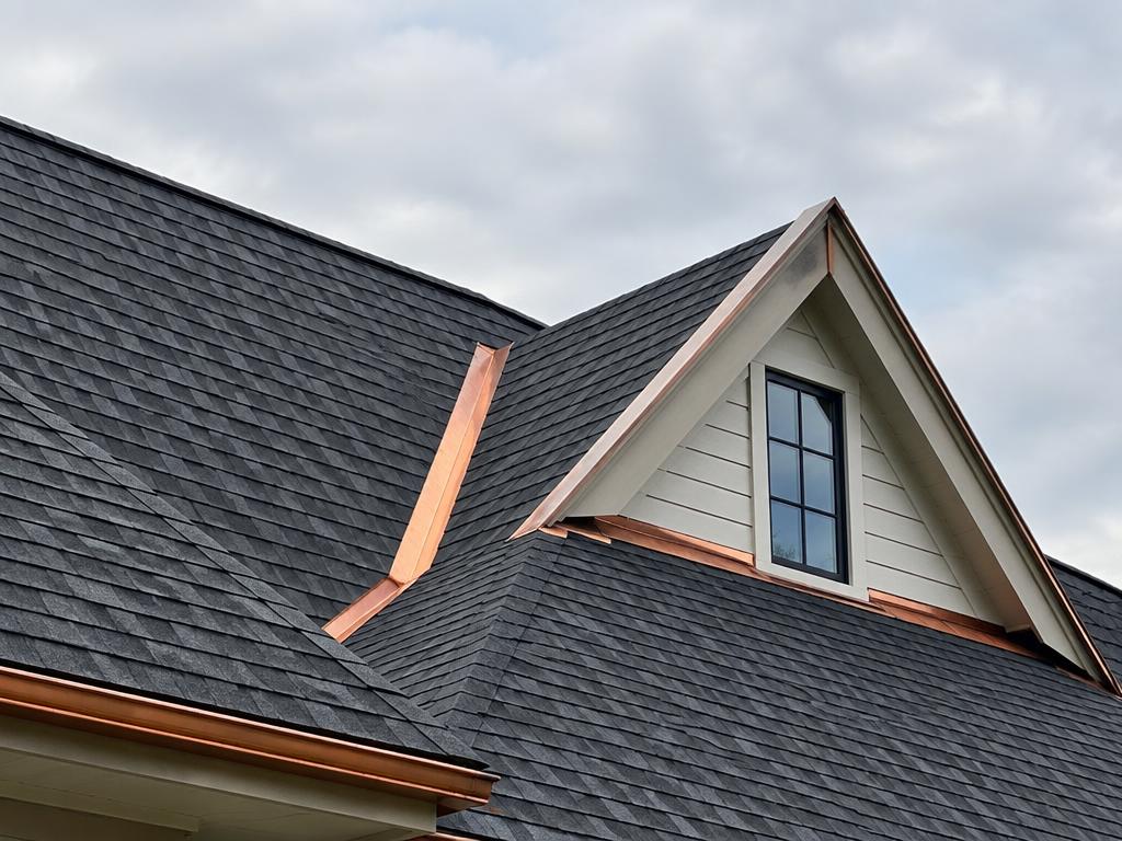 A pitched asphalt-shingle roof with copper flashing